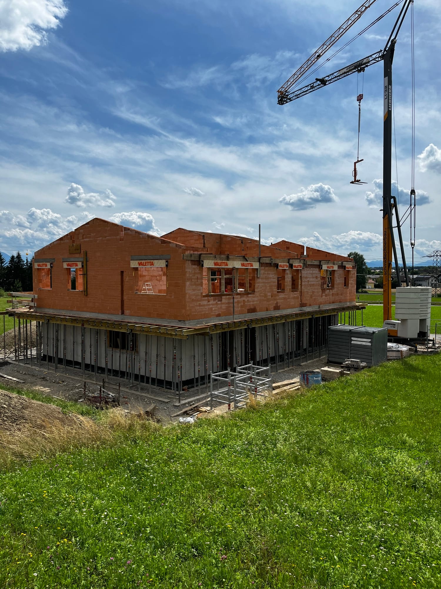 Ziegelrohbau auf einer Wiese unter blauem Himmel