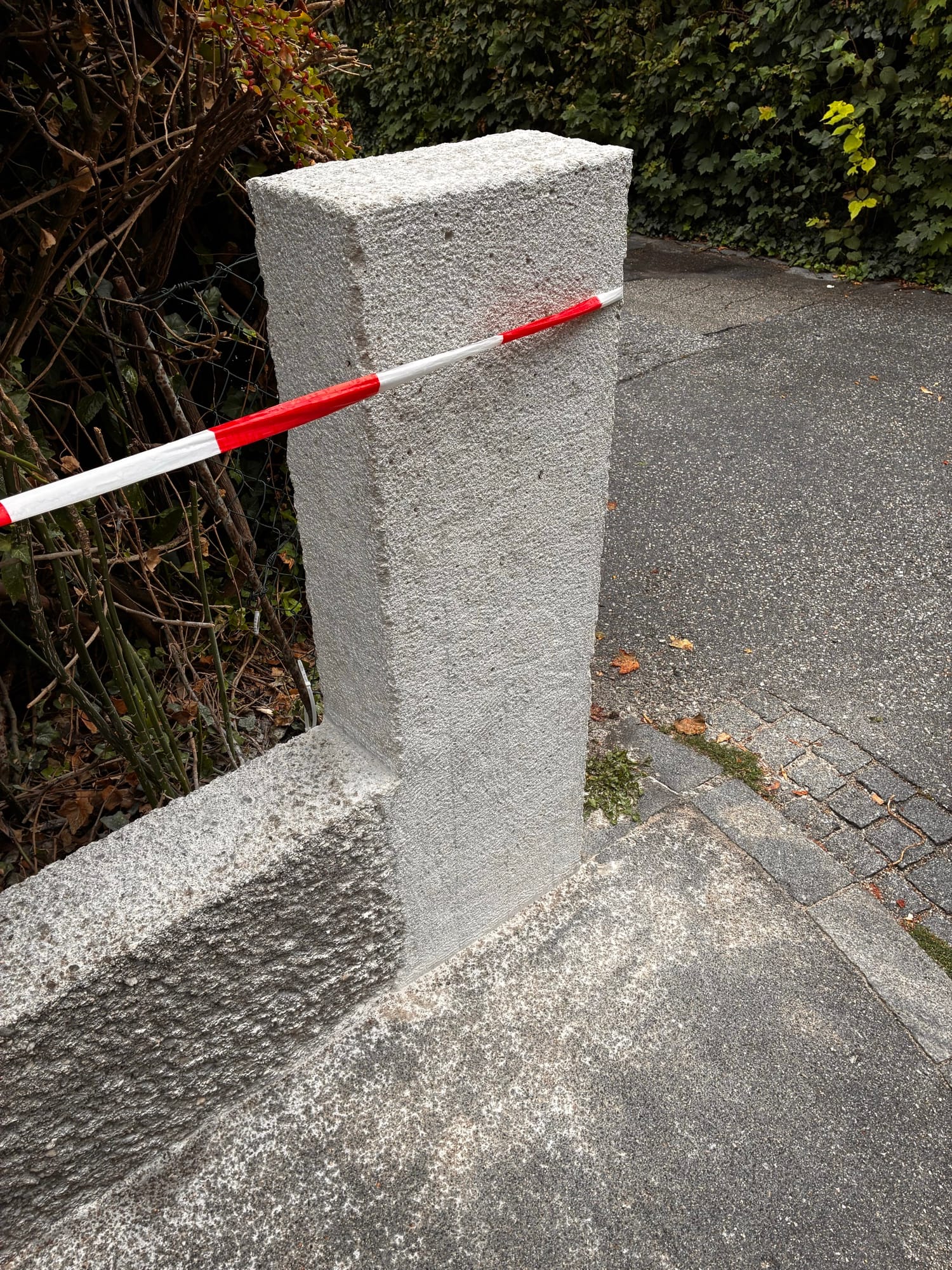 Beschädigter Betonpfeiler an einer Einfahrt, mit Absperrband gesichert
